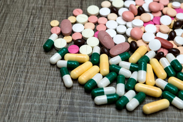 Many colorful pills on a wooden background.