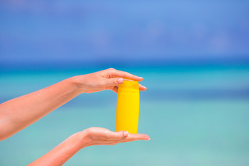 Female hands with suncream bottle background blue sea