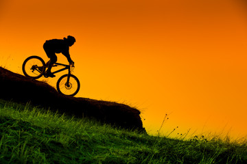 silhouette of downhill mountain bike ride at sunset