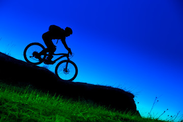 silhouette of downhill mountain bike ride at blue sky