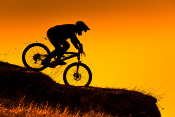 silhouette of downhill mountain bike ride at sunset