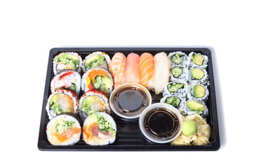 Assorted sushi rolls in a black plastic tray against white backg