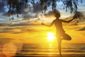 Young woman practicing yoga on the beach at sunset.
