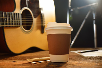 Paper cup of coffee and guitar on wooden table