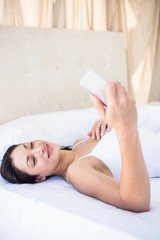 Obraz na płótnie Canvas Pretty brunette using smartphone on bed