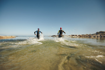 Fototapeta na wymiar Two triathletes rushing into water for swim portion of race