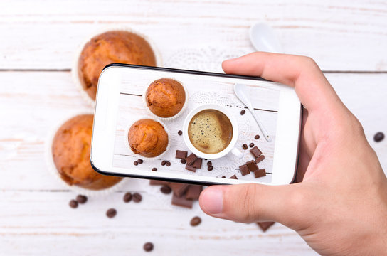 Hands taking photo cup of coffee with muffin with smartphone.