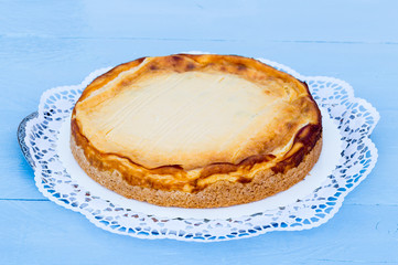Käsekuchen auf blauem Holz mit Tortenspitze