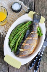 Baked fish with green beans on a wooden table