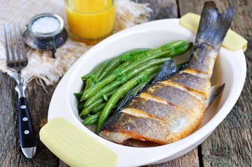 Baked fish with green beans on a wooden table