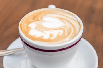 White Cup Of Coffee With Heart Pattern On Wooden Table