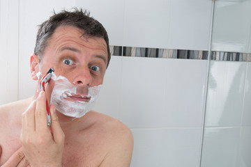 Man shaving with a razor blade and shaving cream in bathroom