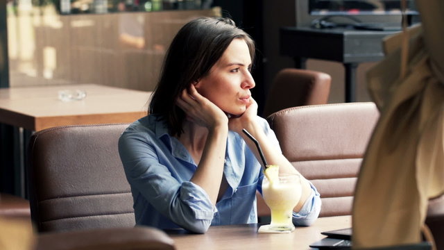 Unhappy, sad woman drinking cocktail sitting in cafe in city