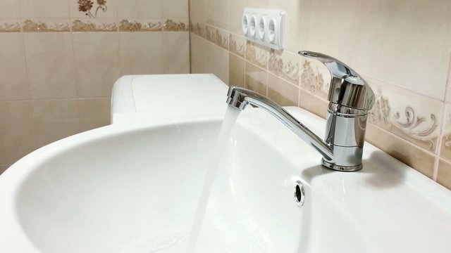 Woman hand opens a water tap in bathroom, then turns water off
