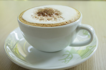 A cup of coffee with heart pattern in a white cup on wooden back