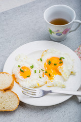 Two fried eggs with chives on white plate