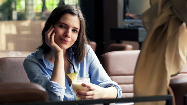 Portrait of happy, young woman holding cocktail sitting in cafe 