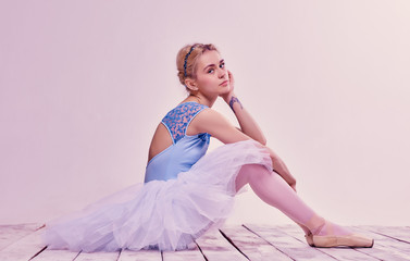 Tired ballet dancer sitting on the wooden floor