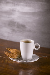 Cup of coffee on plate with croissant on a wooden table.
