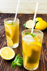 Two glasses of ice tea with ice-cubes on wooden table