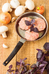 Fresh raw minced meat with basil on a frying pan, on wooden back