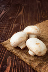 Three white champignons on a burlap on dark wooden table