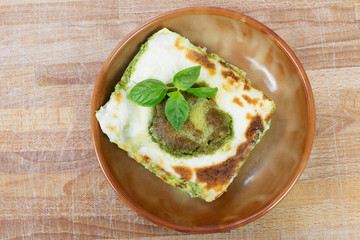 lasagna with pesto inside ceramic bowl over wood