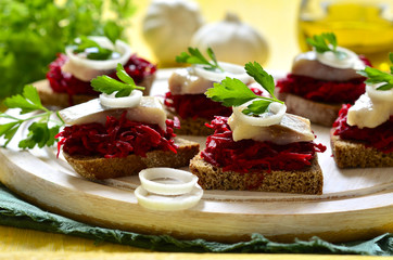 Canape from rye bread with herring slice and beetroot.