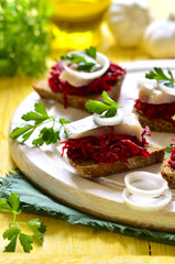 Canape from rye bread with herring slice and beetroot.