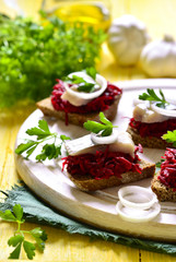 Canape from rye bread with herring slice and beetroot.