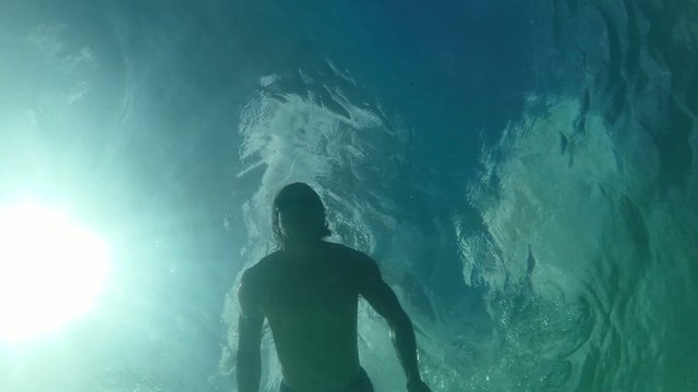 Low angle man swimming on surface of sea backlit by sun