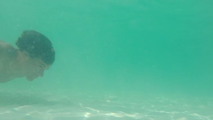 Man swims underwater over sandy sea bottom