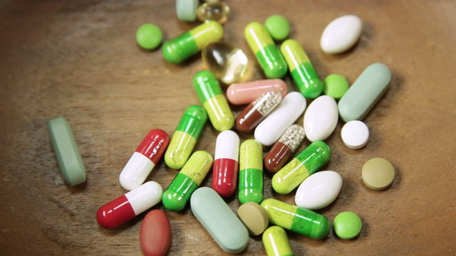 Assortment of colorful pills accumulating in wooden bowl