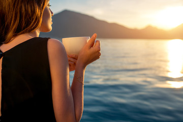 Young woman drinking coffee on the pier at sunrise