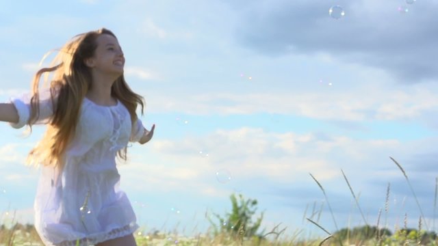 Happy girl with long hair catching soap bubbles outdoor