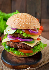 Big juicy hamburger with vegetables and beef on a wooden table