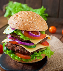 Big juicy hamburger with vegetables and beef on a wooden table