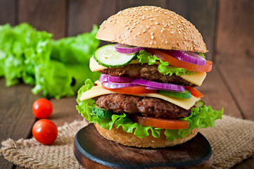 Big juicy hamburger with vegetables and beef on a wooden table