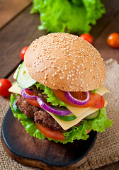 Big juicy hamburger with vegetables and beef on a wooden table