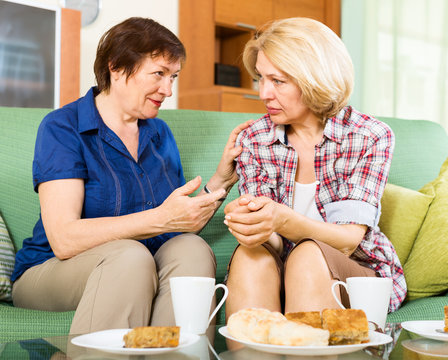 Two Sad Aged Women Talking On Couch