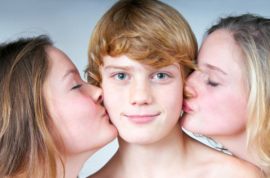 Zwei Mädchen küssen Jungen auf Backe