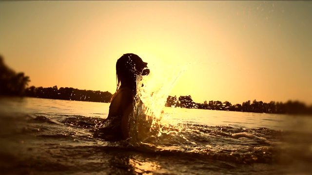 Teen girl swimming and splashing on summer beach over sunset