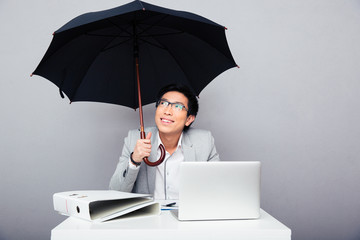 Happy businessman sitting at the table with umbrella