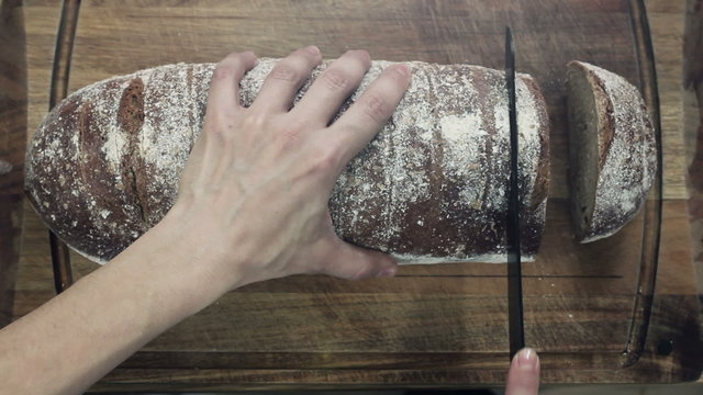 Slicing whole grain bread on wooden table, top view