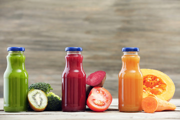 Glass bottles of fresh healthy juice with set of fruits and vegetables on wooden background