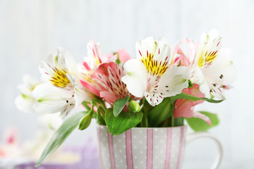 Beautiful flowers in cup, on wooden background