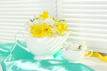 Beautiful bouquet of yellow daffodils and roses in teapot on windowsill