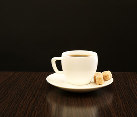 Cup of coffee with lump sugar on wooden table, on dark background