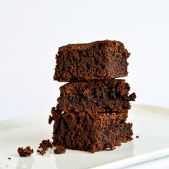 A small tower of chocolate brownies served on a square plate.