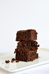 A small tower of chocolate brownies served on a square plate.